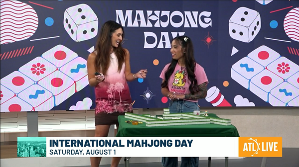 Krizia Cato and host Savannah Louie standing at a mahjong table on the Atlanta News First set during a live International Mahjong Day segment